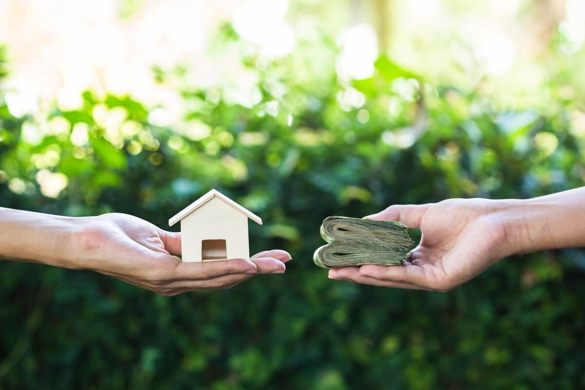 a wooden model of a house in the palm of his hand and money in another hand