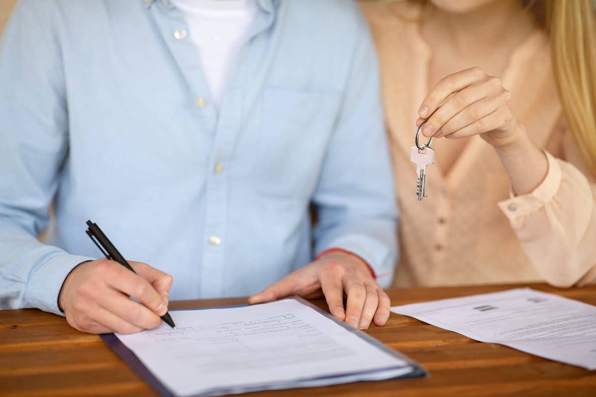 A man signing a real estate contract and an agent holding a key