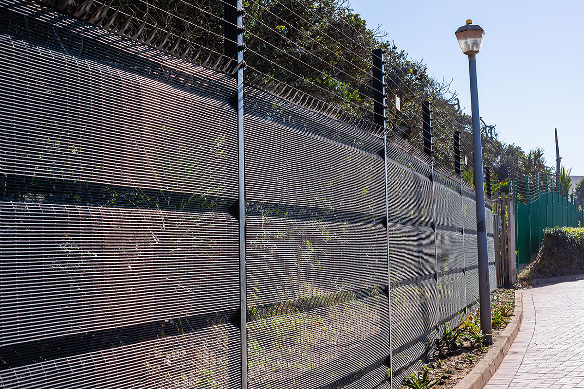 Tall security fence with razor wire along an urban path.
