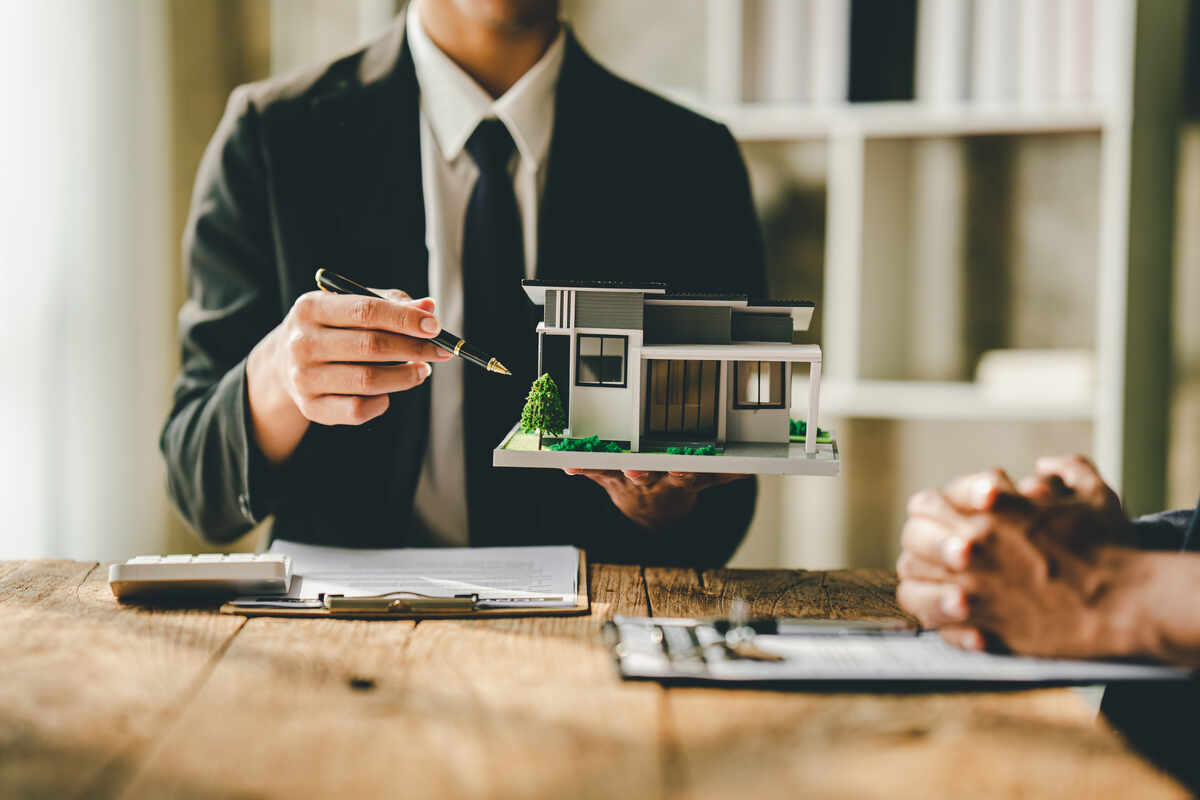 real estate agent holds a model of a house in one hand and a pencil in the other